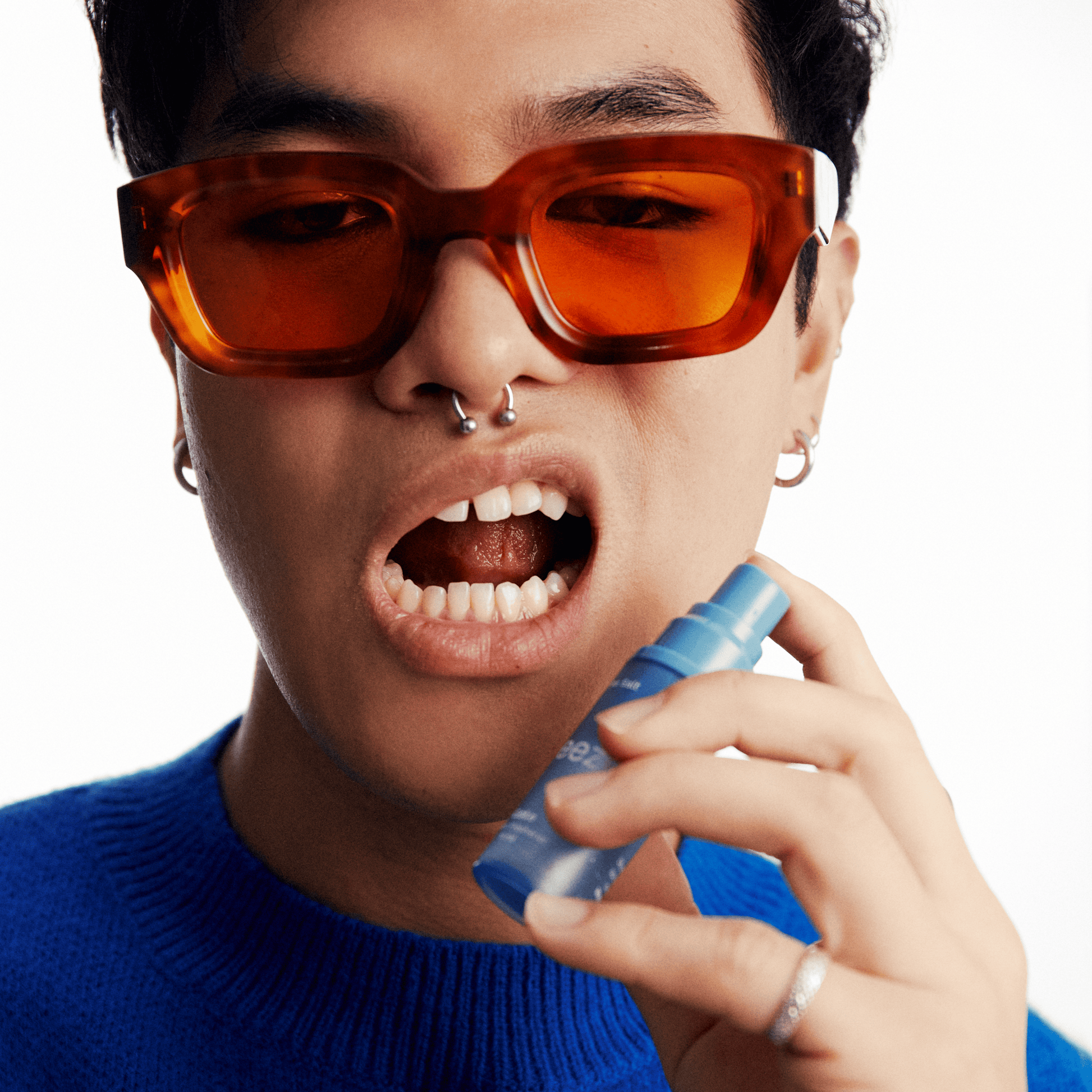 Person wearing orange sunglasses and a blue sweater, holding a blue can.