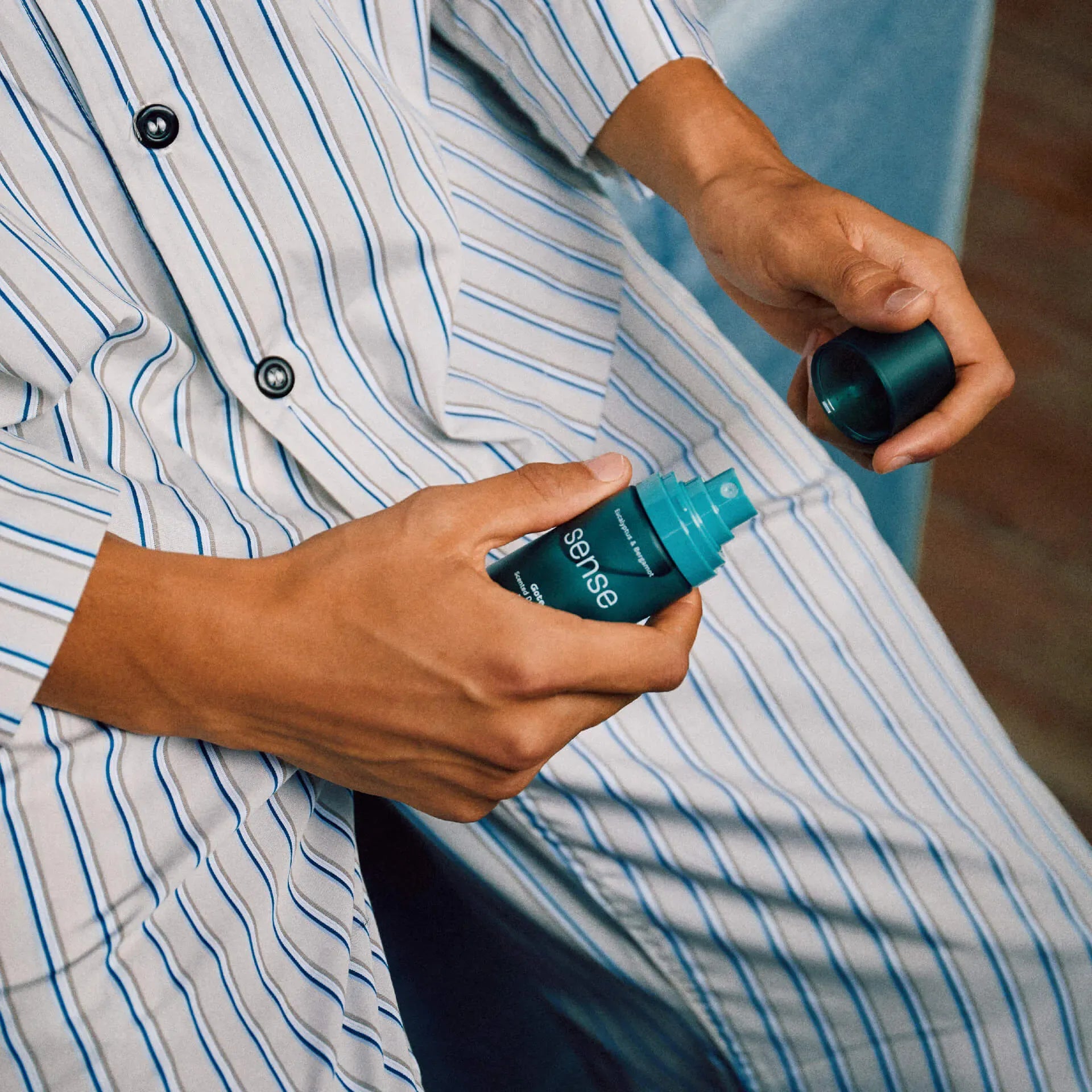 Person holding a bottle of 'sense' spray against a blurred background