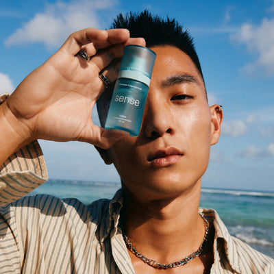Person holding a 'sense' deodotant against a beach background