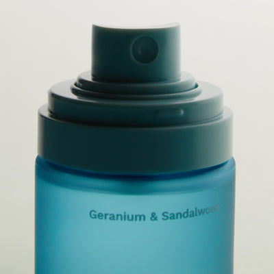 Close-up of a blue spray bottle cap with the text 'Geranium & Sandalwood' on the bottle body.