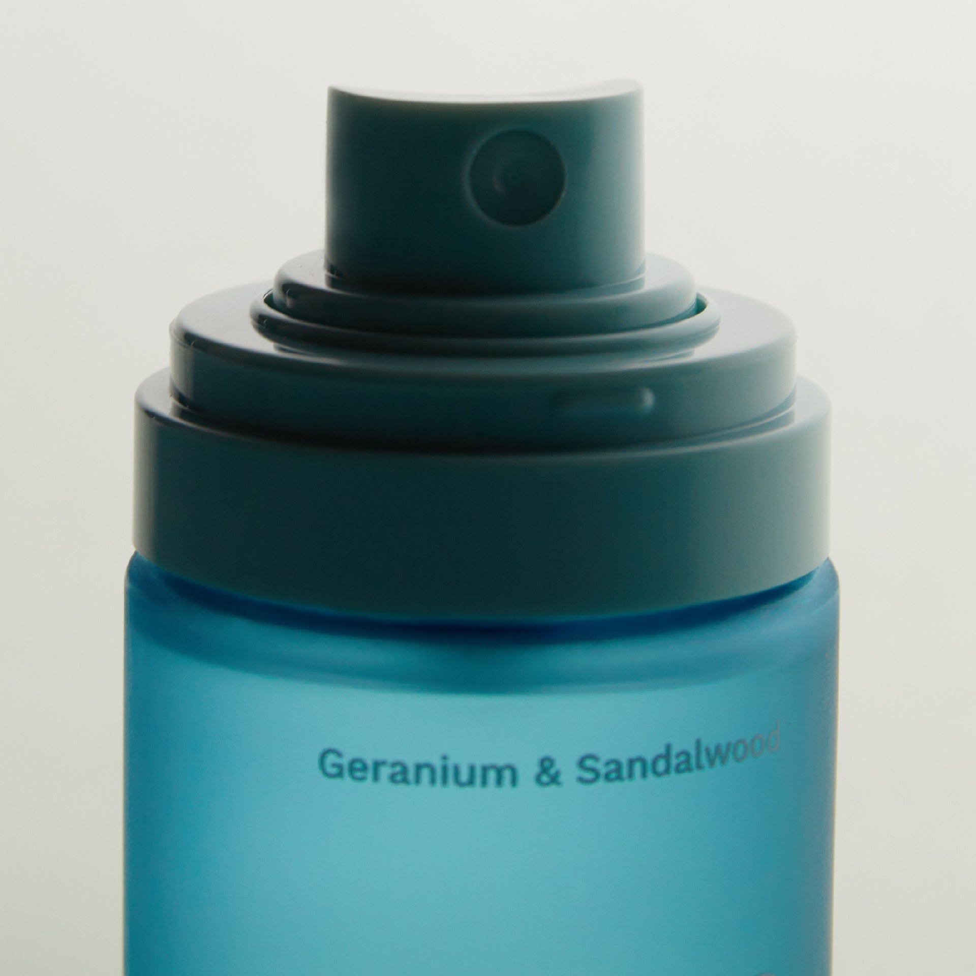 Close-up of a blue spray bottle cap with the text 'Geranium & Sandalwood' on the bottle body.